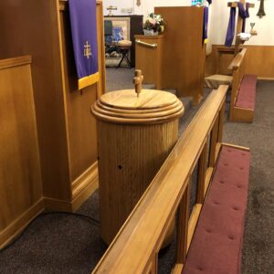 Oak baptismal with lid parked behind Communion rail when not being used.